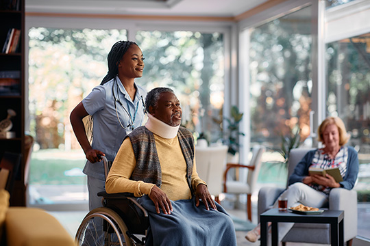 nurse helping a man in a wheel chair and with a brace around his neck in a care home